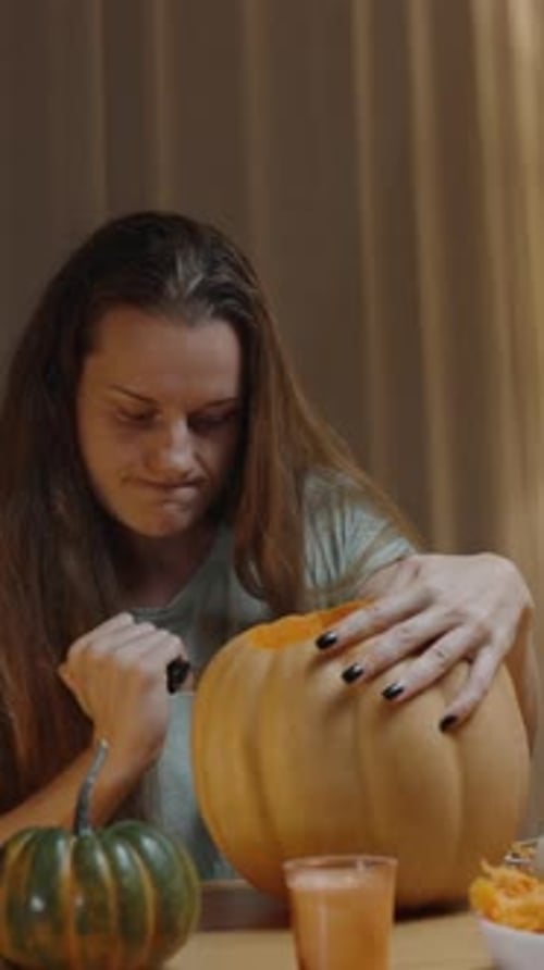 Vertical video. Young Woman with a Stern Face Carving a Jack-o'-Lantern from the Pumpkin, Struggling
