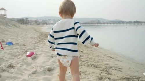 Adorable toddler boy happily playing with a shovel on the sandy beach