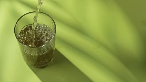 Pouring Refreshing Bubbly Drink Into Glass on Green Background