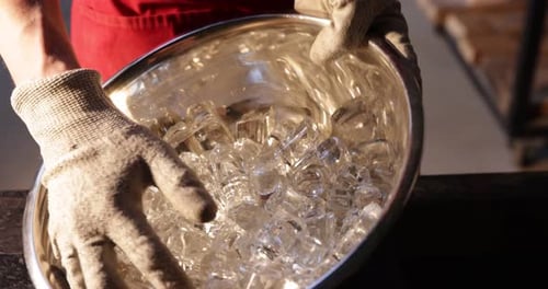 Worker with bowl of molten glass pieces at table in workshop, closeup