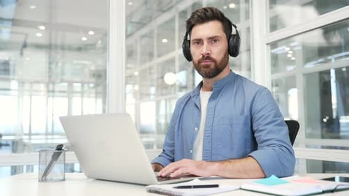Man Working on Laptop with Headphones in Office