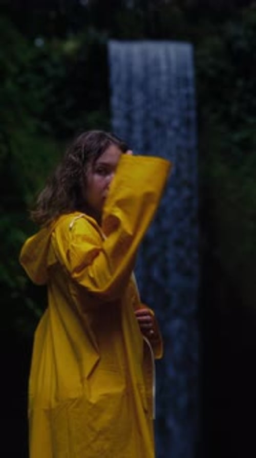 Woman in Yellow Raincoat Posing By Waterfall
