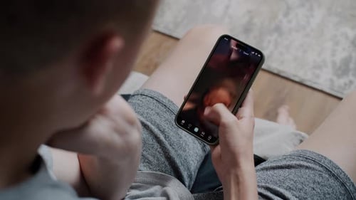 Teen Boy Scrolls Through and Watches Social Network Feed with Short Videos Using Phone