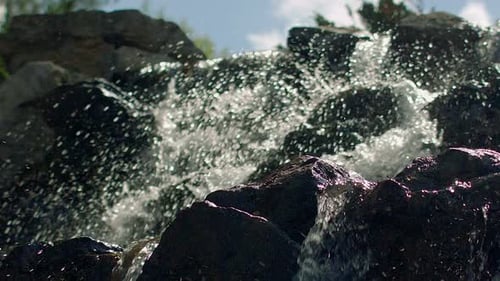 Mountain waterfall splashing on stones in slow motion on a sunny summer day