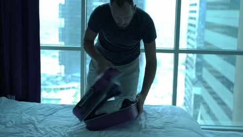 Young Man Packing Suitcase on Bed and Leaving Hotel Room 30s