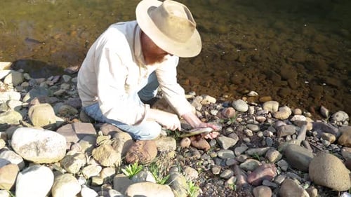 A bushman prepares a brown trout by the side of a river in the Australian high country.