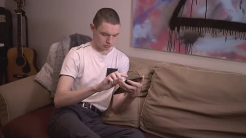 Young Man Sitting On The Sofa, Holding And Scrolling On His Electronic Tablet. Device. - close up sh
