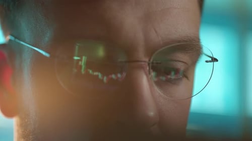 Trader Wearing Glasses is Working on Laptop Computer Screen with Stock Market Charts and Bitcoin BTC