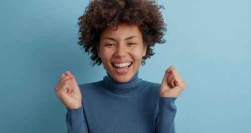 Cheerful Glad Afro American Woman Wears Casual Turtleneck Does Winner Gesture Clasps Hands And Sm...