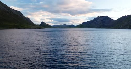 Low flight over water surface of fjord in Norway with mountain in background. Aerial drone at sunset