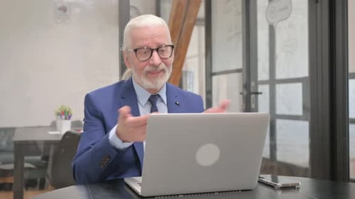 Senior Man Video Chatting on Laptop in Office
