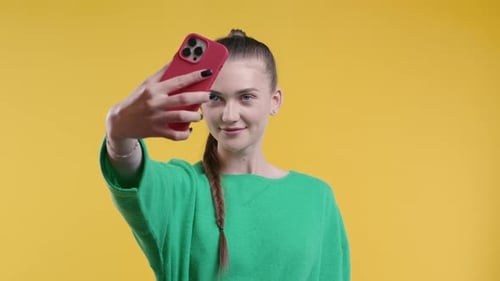 Woman Takes Selfie with Phone on Yellow Background