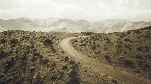 Route de terre sinueuse à travers les montagnes du Pamir au Tadjikistan sous un ciel nuageux