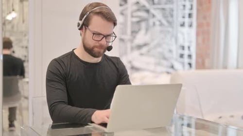 Man with Headset Typing on Laptop Indoors