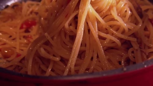 Slowmotion close up video of serving of spaghetti with a fork from the cooking pan to the plate