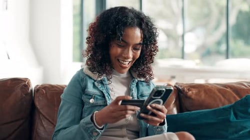 Woman Smiles, Using Phone with Credit Card on Couch