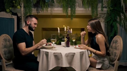 A young couple is sitting in an expensive restaurant having dinner trying dishes drinking wine love