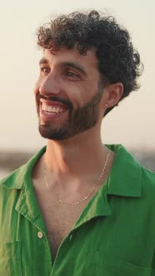 Un gars à la barbe vêtu d'une chemise verte rit et parle à quelqu'un