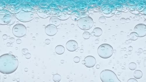 Bolhas azuis transparentes se formam e flutuam em direção a outras em uma superfície transparente sobre fundo azul O