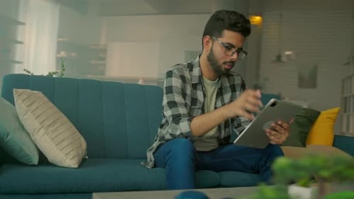 Young Adult Uses Tablet on Couch Indoors