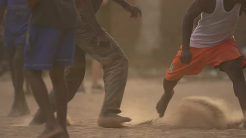 Barefoot boys playing soccer in a dusty area