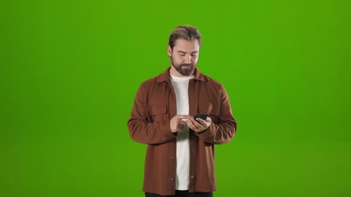 Man Standing Over Green Background with Mobile in Hands