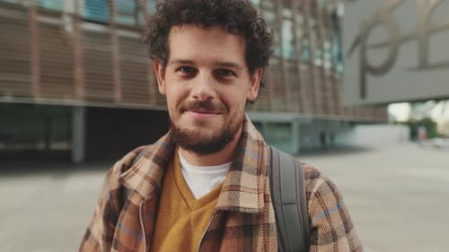 Close up, guy student stands outside the university looks at the camera and smiles