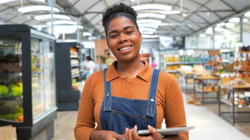 Smiling African American Saleswoman Holding Tablet in Grocery Store