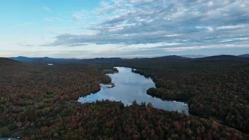 Rio cercado por denso matagal com folhagem de árvores de outono durante o pôr do sol. Foto aérea ampla