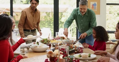 Família extensa comemorando a refeição natalina esculpindo perus passando pãezinhos servindo salada na mesa de jantar