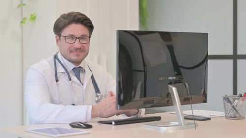 Middle Aged Doctor Smiling at Camera while Working on Laptop in Clinic