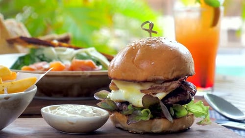 Cheeseburger with Crispy Bacon and Fresh Vegetables Served Outdoor Restaurant