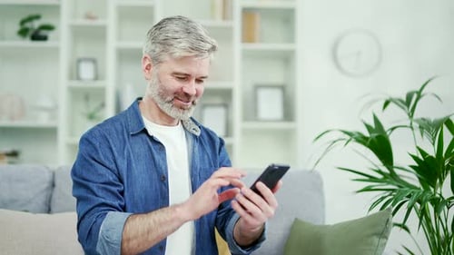 Mature Man Using Smartphone on Sofa at Home