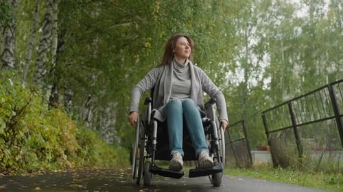 Woman with Injury Moves Turning Wheels of Wheelchair in Park