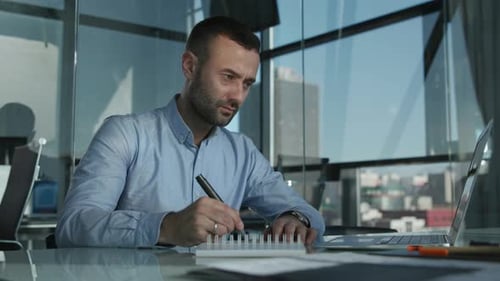Man Writing in Notebook at Desk in Office