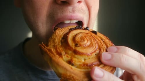Man Bites Into Pastry with Raisins, Close Up