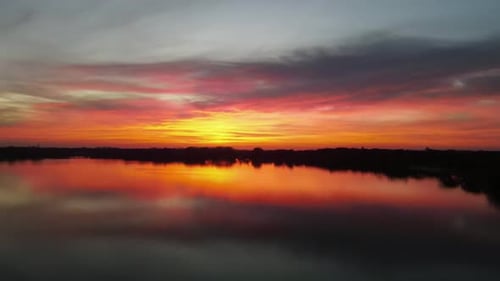 Toma aérea de una vibrante puesta de sol sobre un lago. Reflejo de colores en el agua.