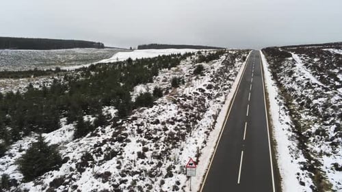 Luftbild folgt einer langen, leeren Straße in die Ferne über verschneite Hochlandmoore