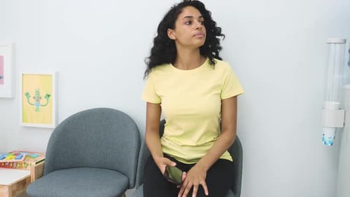A nervous young woman waits nervously in the waiting room of a medical clinic for her name