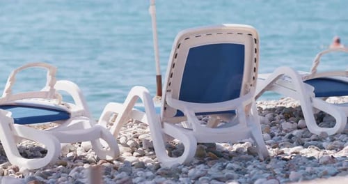 Sunbeds for tourists stand on pebble beach of ocean coastline