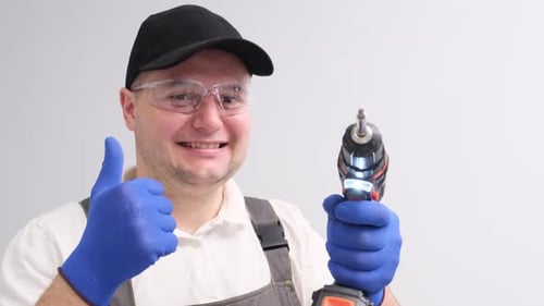 Portrait of a Man in a Special Construction Suit and with a Drill in His Hands He Shows a Thumb Up