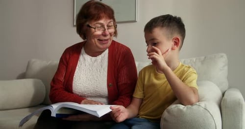 Grandmother Reading with Grandson on Couch Indoors