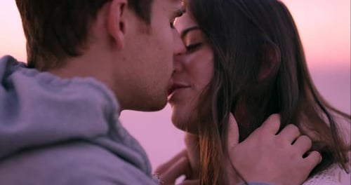 4k video footage of a young couple kissing on the beach at sunset