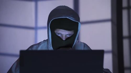 Hacker in Mask Uses Laptop in Dark Office