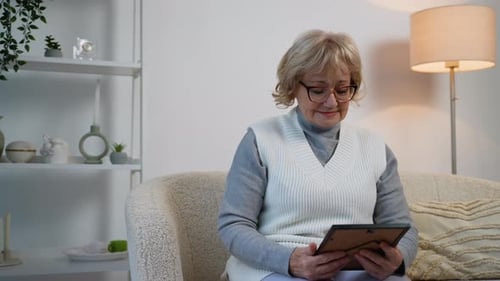 Senior Woman Looks Thoughtfully at Framed Photo