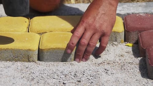 Person Laying Yellow Paving Stones with Mallet