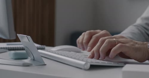 Closeup of Male Hands Using Computer Keyboard Typing Working at Desk in Office