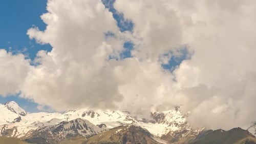 Timelapse shot of Snowy Mountain Range Under Blue Sky With Dramatic Clouds and Alpine Peaks