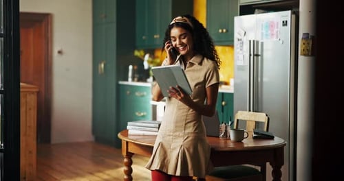 Woman Holding Tablet Talking on Phone in Kitchen
