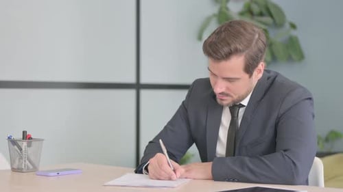 Man Writing at Desk in Modern Office